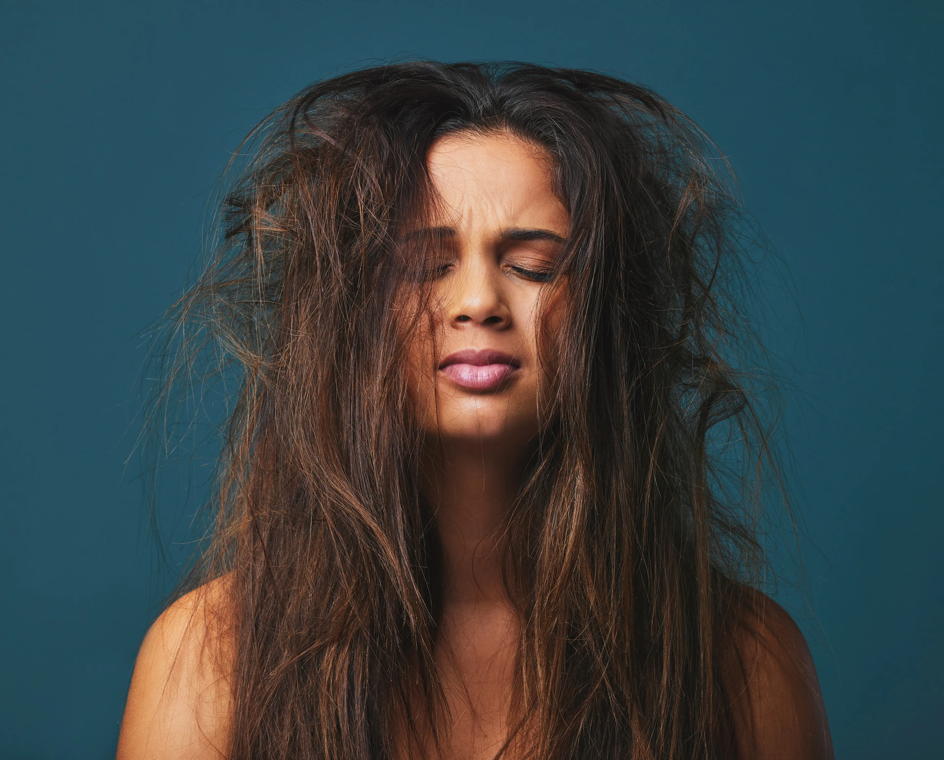 Studio shot of a beautiful young woman with messy hair posing against a blue background Studio shot of a beautiful young woman with messy hair posing against a blue background